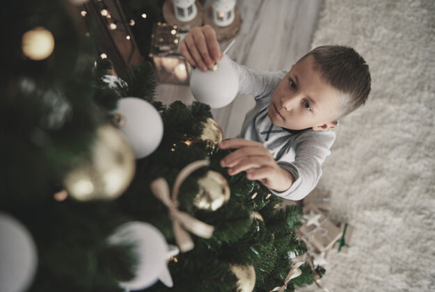 站立头顶上穿着睡衣的男孩正在准备一棵圣诞树家里室内圣诞节时间圣诞树
