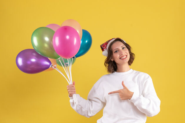 前面黄色墙壁上手持彩色气球的年轻女子的正视图气球装饰年轻