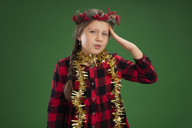 检查戴着圣诞花环的小女孩穿着格子裙 脖子上缠着金属丝 把手误放在头上脖子手女孩