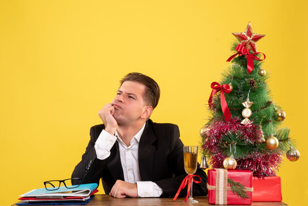 年份正面图年轻的男工人坐在圣诞礼物和树上紧张地思考圣诞颜色年轻