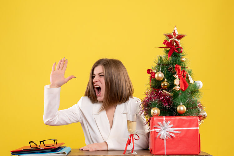 职业正面图：女医生坐在黄色背景的桌子前 带着圣诞树和礼品盒背景健康电脑