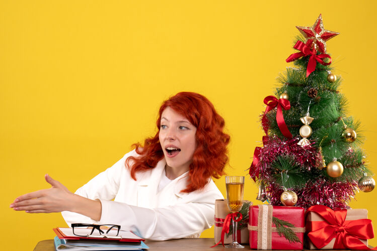 人女工人坐在桌子后面 手里拿着圣诞礼物和黄色的圣诞树工人成人黄色