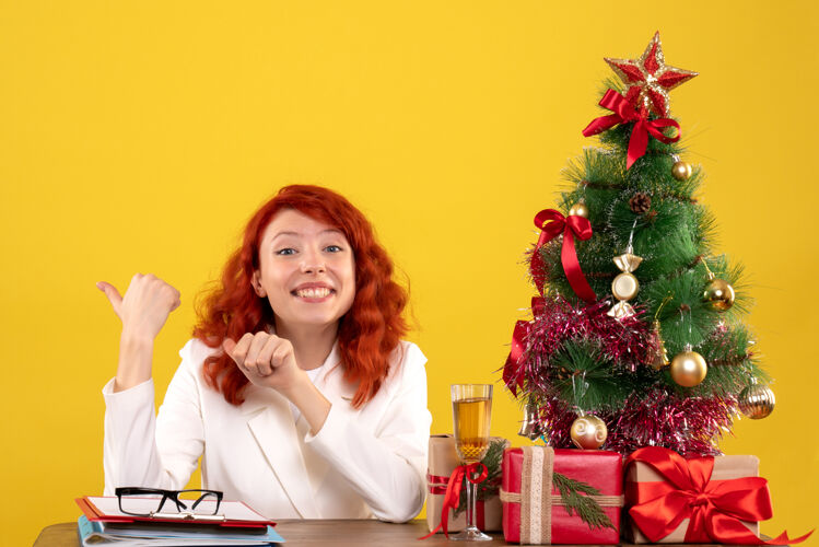 圣诞节女工人坐在桌子后面 黄色的是礼物和文件安排人工人