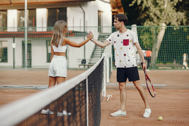 球网球场上的一对年轻夫妇两个穿着运动服的网球运动员运动球拍运动员