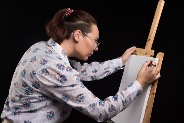 铅笔女画家用铅笔在画布上画一幅画 背景是黑色的画布成人手