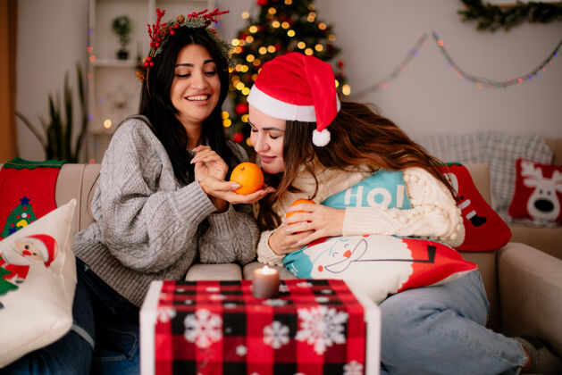 高兴可爱的年轻女孩戴着圣诞帽 坐在扶手椅上嗅橘子 在家里享受圣诞时光扶手椅享受时间