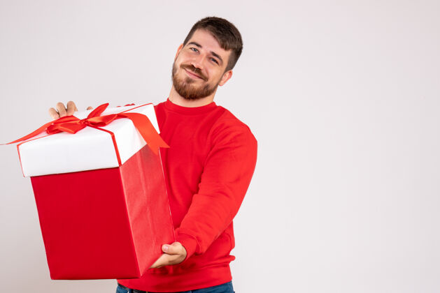 前面身穿红衫的年轻人在白色墙上的盒子里拿着圣诞礼物的正视图情感快乐举行