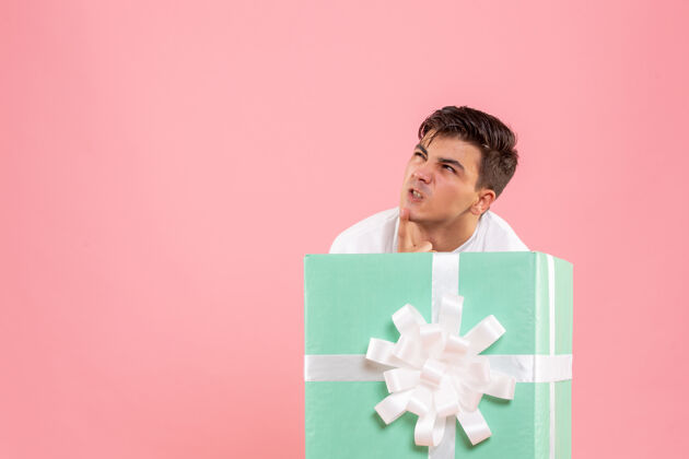 礼物隐藏在粉红色墙上的礼物里面的年轻人的正面视图十二月盒子礼品盒