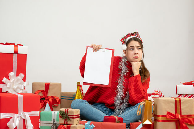 举行戴着圣诞帽的悲伤女孩拿着文件围坐在白色的礼物上悲伤的女孩礼物悲伤