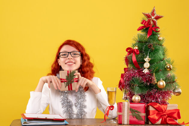 圣诞节前视图：女医生坐在桌子后面 黄色背景上有圣诞礼物花女医生情绪