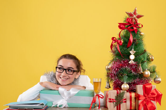 树正面图女医生围坐在圣诞礼物和黄色背景上微笑的圣诞树旁人周围医生