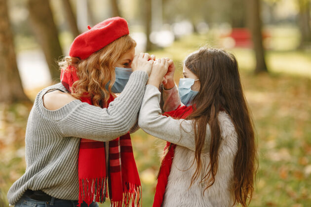 护理秋天公园里的一家人冠状病毒主题母亲带女儿围巾安全树叶