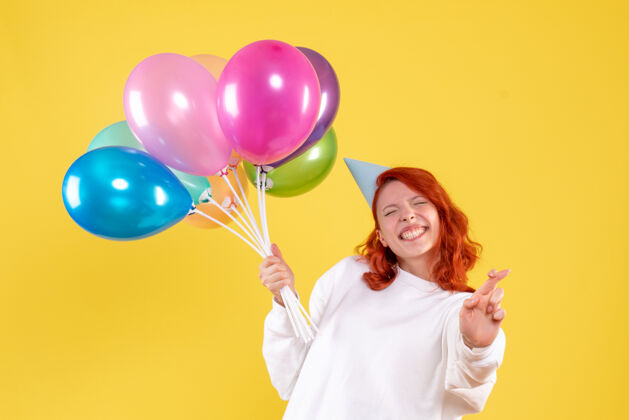 快乐黄色墙壁上手持可爱彩色气球的年轻女子的正视图生日年轻的女性前面