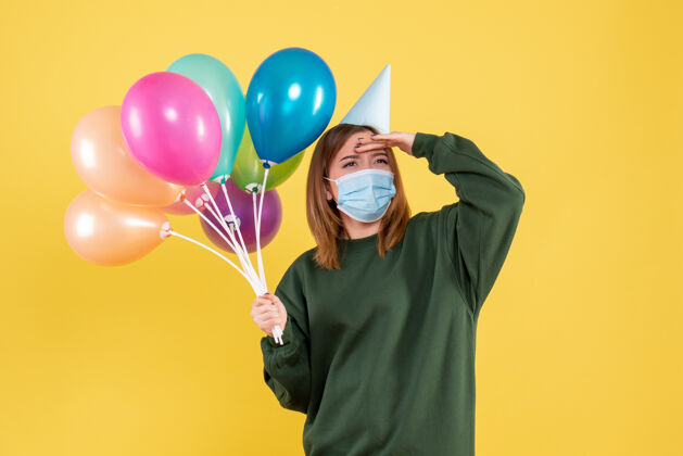 年轻正面图戴面具的年轻女性手持五颜六色的气球光明病毒气球