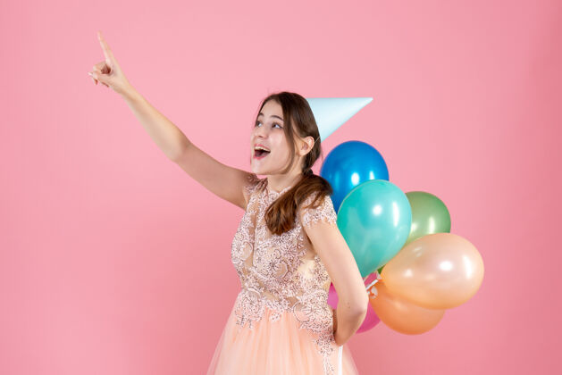 派对快乐的派对女孩 戴着派对帽 背着气球 手指指着粉色的东西漂亮快乐气球