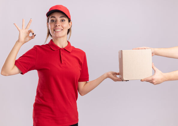 手微笑着的年轻漂亮的女送货员 穿着制服 手势表示同意 并将名片盒交给一个孤立的人手势微笑人