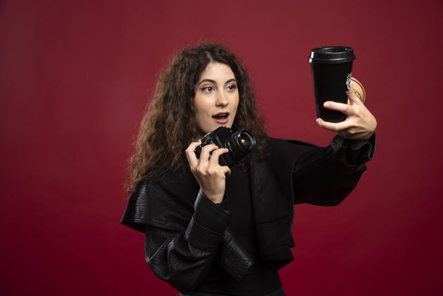 深色一个穿着全黑衣服的年轻女人手里拿着一个杯子和一个照相机装束外卖照片