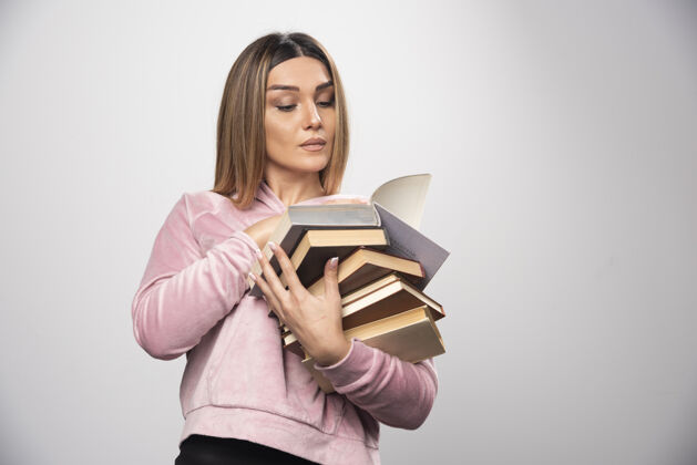 女性穿着粉色运动衫的女孩手里拿着一堆书 打开上面的一本读着学习教育人