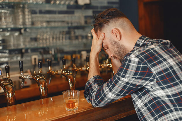 帅哥一个穿衬衫的男人手里拿着一个玻璃杯那个家伙正坐在酒吧里 抱着他的头饮料成人酒吧