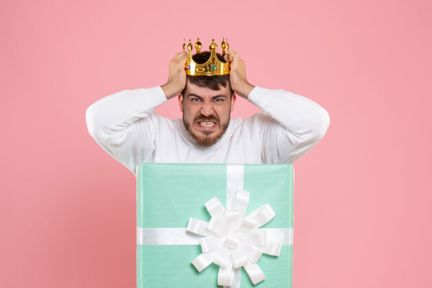 盒子粉红色墙上戴着王冠的礼物盒内年轻人的正面图情感微笑丝带