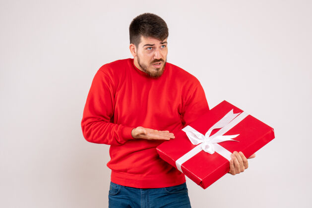 前面一个穿着红衫的年轻人拿着圣诞礼物站在白色的墙上年轻微笑礼物