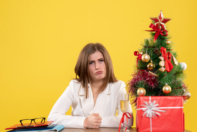 办公室正面图：女医生坐在黄色背景的桌子前 放着圣诞树和礼品盒女性前面女医生