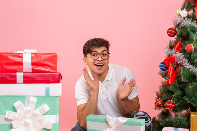 圣诞快乐年轻人围着礼物和粉红色墙上的圣诞树的正视图成人正面人