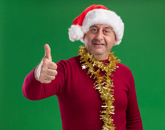 微笑中年男子戴着圣诞老人帽 脖子上戴着金属丝 脸上挂着微笑 竖起大拇指显示看周围