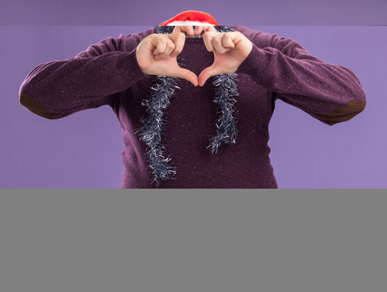 脖子中年男子戴着圣诞老人帽 戴着防护面具 脖子上戴着金属丝花环 戴着眼镜 在紫色的墙上做着心形标志男人金属丝中年