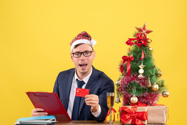 黄色前视图的商人显示卡坐在圣诞树附近的桌子上 黄色的礼物商务礼物男性