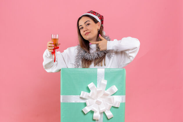人前视图的年轻女子庆祝圣诞节与饮料上粉红色的墙壁礼物年轻女性聚会