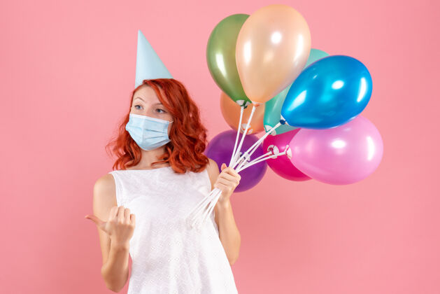 乐趣前视图中的年轻女子拿着五颜六色的气球在无菌面具上粉红色的墙壁无菌快乐女性