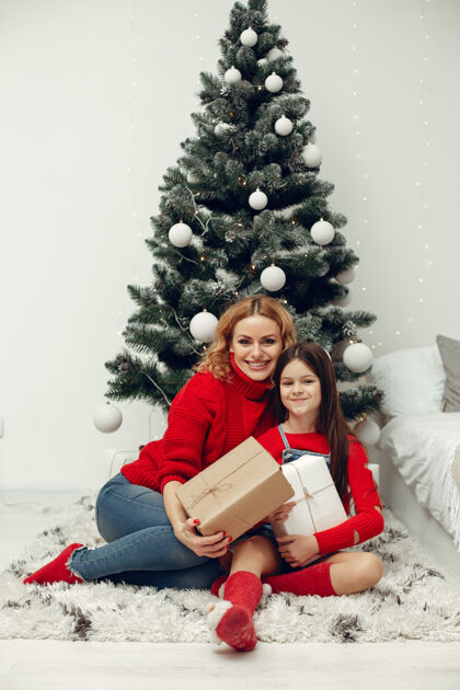 节日人们在为圣诞节做准备母亲在和女儿玩耍一家人在节日的房间里休息孩子穿着红色毛衣亮光亮光童年