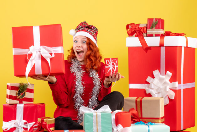 盒子坐在黄色墙上的圣诞礼物周围的年轻女子的正视图年轻购物礼物