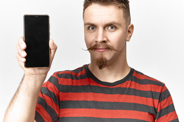 手机漂亮漂亮的年轻无胡须的欧洲男性 穿着条纹t恤 手持普通黑色手机 空白显示 可为您的文本 模板或广告提供复制空间技术微笑演示