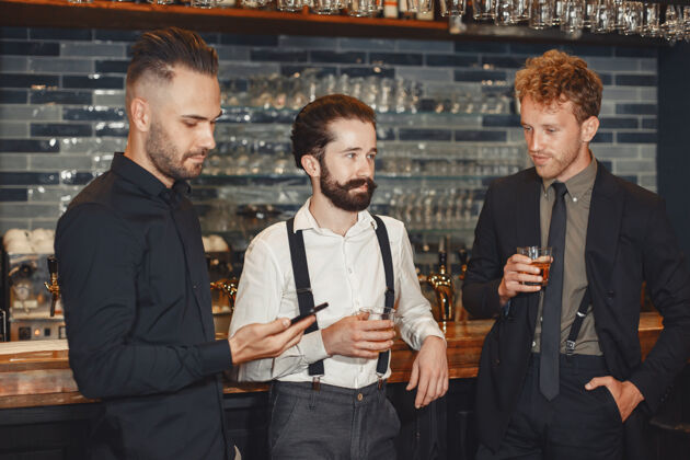 足球和最好的朋友见面三个穿着休闲服的快乐的年轻人一起坐在酒吧里聊天喝啤酒男人手里拿着电话会议伙伴酒吧