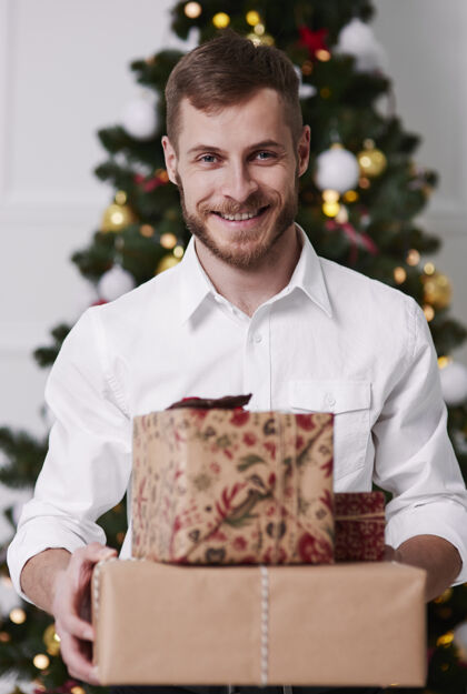举行带着一堆礼物的兴奋男人的画像圣诞节微笑房子