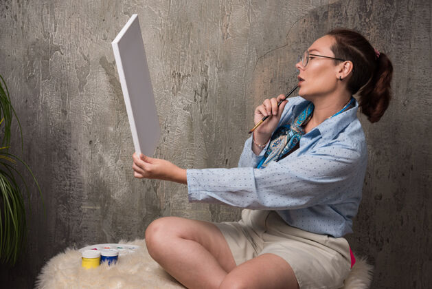 人女人坐在画布上 看着大理石背景上的画笔女人女士女性