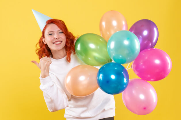 年轻的女性黄色墙壁上手持彩色气球的年轻女子的正视图聚会快乐女人