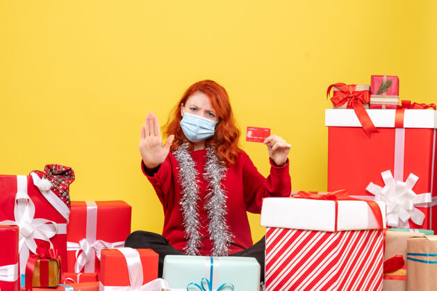 银行正面图是一位年轻女子戴着面具围坐在礼物旁边 黄色的墙上挂着银行卡前面年轻人圣诞节