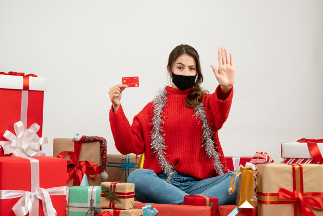 年轻女孩带着红色毛衣和黑色面具的年轻女孩拿着卡片围坐在白色的礼物上年轻人黑色礼物
