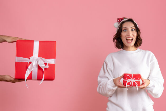 微笑年轻女子拿着小礼物 在粉红色的墙上接受男人的礼物小女人圣诞节