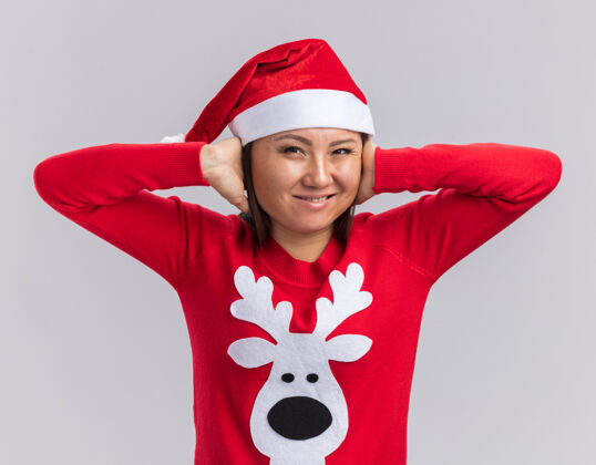女孩恼怒的亚洲小女孩戴着圣诞帽 戴着毛衣 耳朵被隔离在白色背景上毛衣圣诞节耳朵