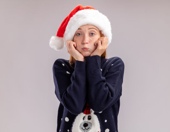 眼镜悲伤的年轻漂亮女孩戴着圣诞帽戴着眼镜把双手放在脸颊上隔离在白色的背景上悲伤脸蛋女孩