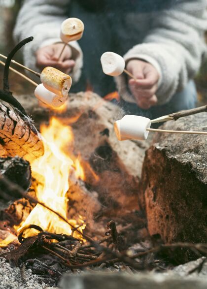 户外在营火中烧棉花糖的年轻女人冬天火放松