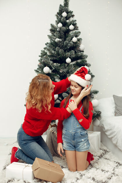 圣诞老人人们在为圣诞节做准备母亲在和女儿玩耍一家人在节日的房间里休息孩子穿着红色毛衣杉木帽子光泽