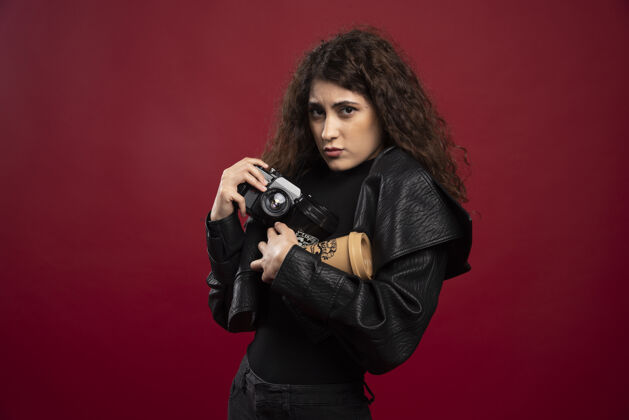 摄影师一个穿着全黑衣服的年轻女人手里拿着一个杯子和一个照相机外卖外卖时尚
