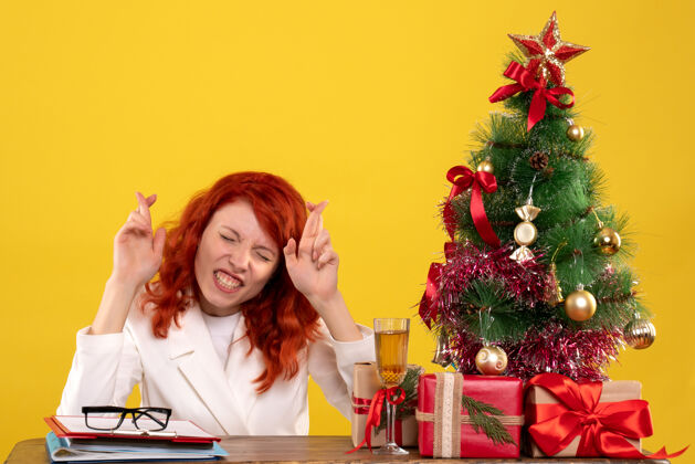 礼物女工人坐在桌子后面 手里拿着圣诞礼物和黄色的圣诞树坐着圣诞插花