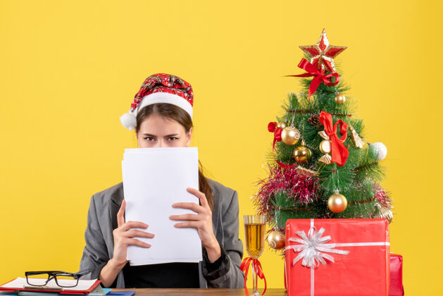 文件正面图：戴圣诞帽的年轻女孩坐在桌旁 脸上贴着圣诞树和鸡尾酒礼物女孩年轻女孩坐