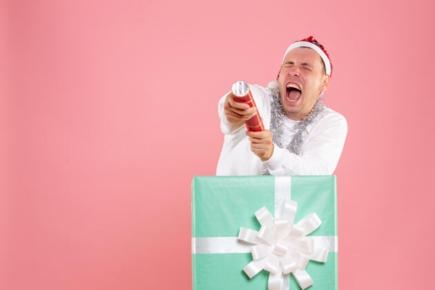礼品盒年轻人在粉红色墙上放鞭炮的正面图圣诞快乐脸粉色